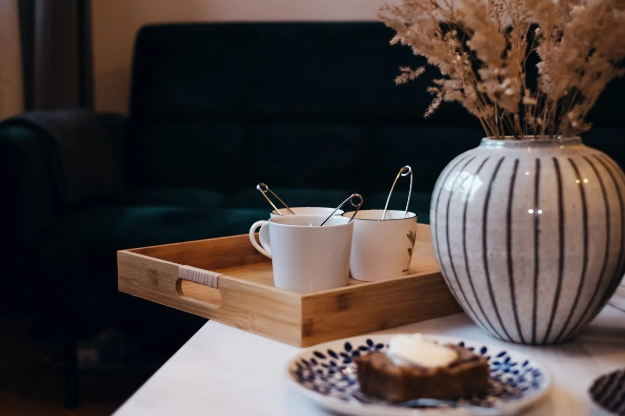 Warm indoor setting featuring coffee cups, cake, and a decorative vase on a wooden tray.