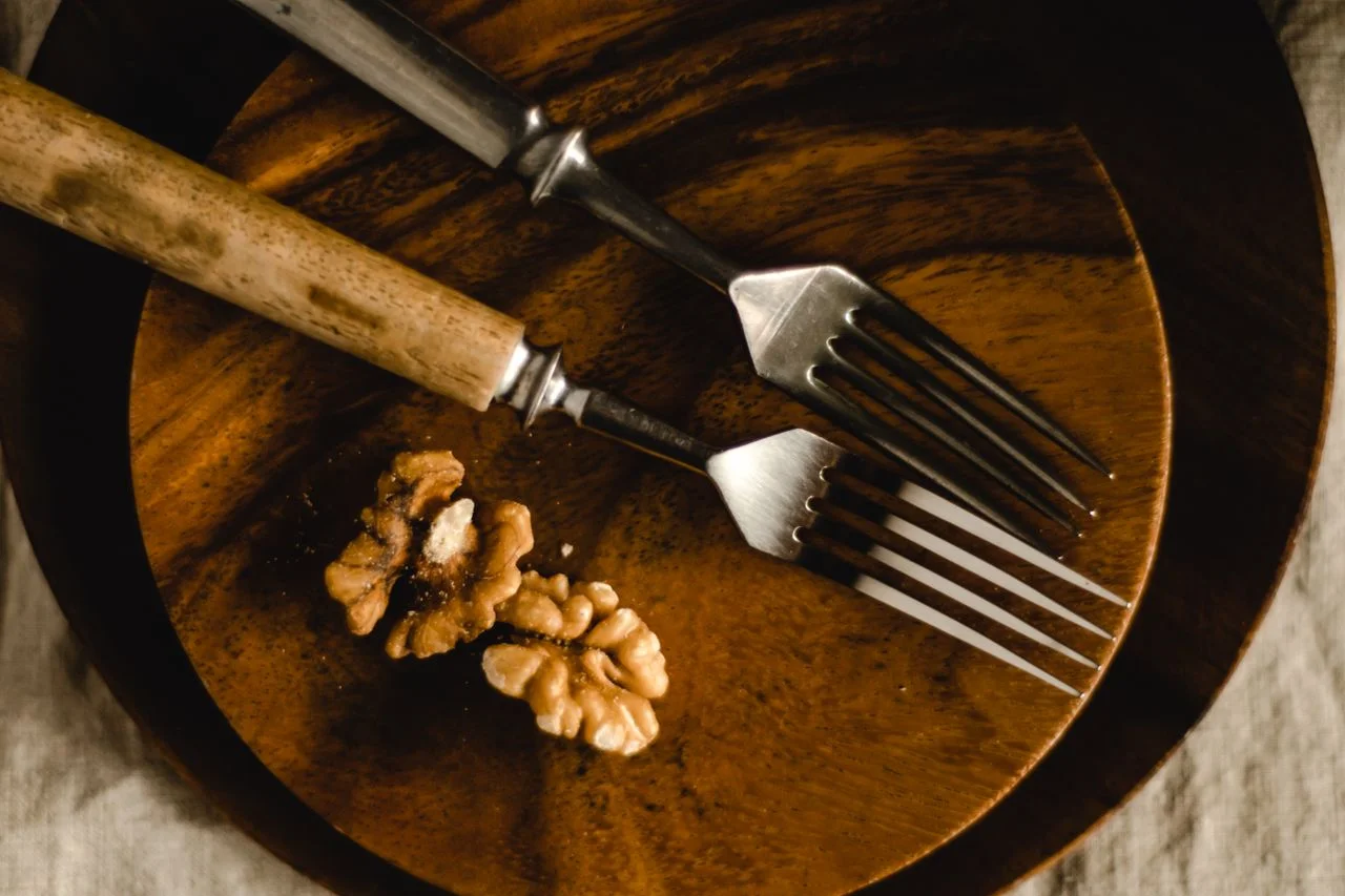 our-experience A close-up of forks and walnuts on a rustic wooden plate, showcasing a simple still life.
